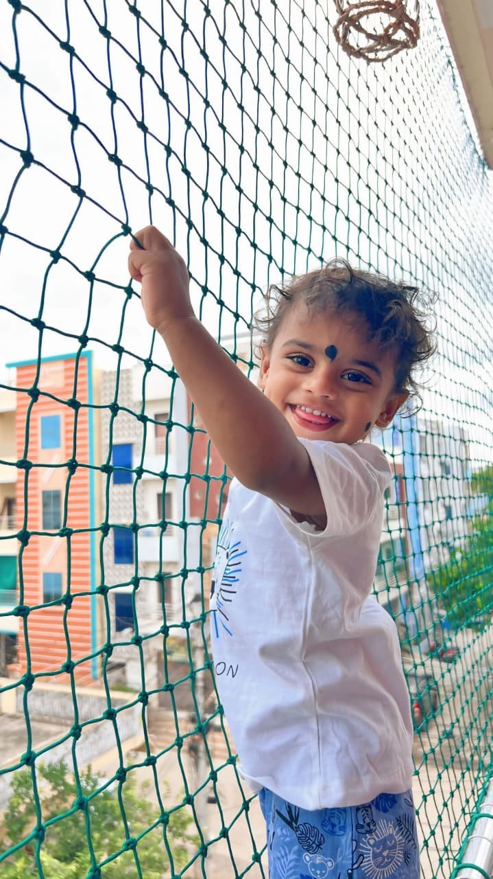 Smiling child holding a green balcony safety net